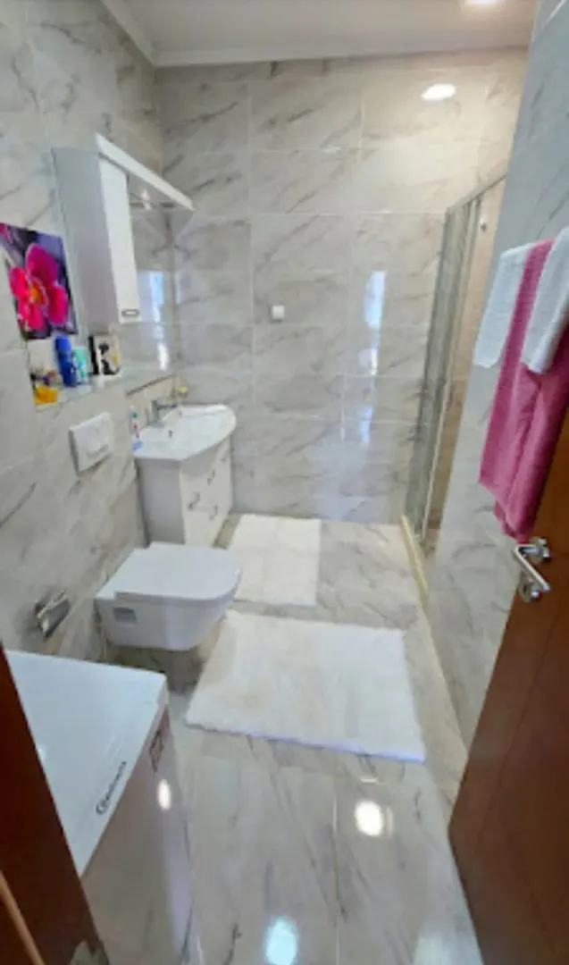 Kupatilo obloženo keramičkim pločicama sa tuš kabinom, umivaonikom i wc šoljom.