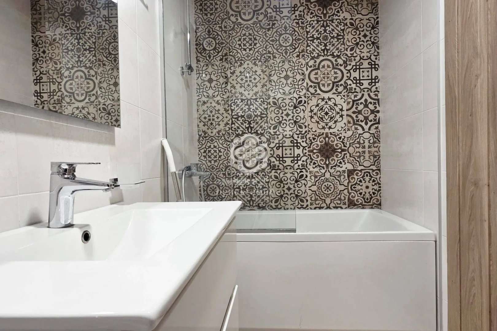 Modern bathroom with a washbasin and a bathtub decorated with patterned tiles.