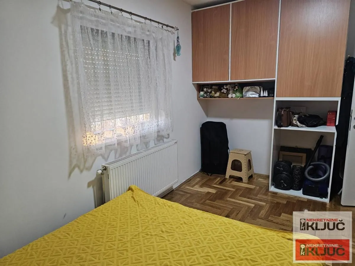 Manja spavaća soba sa krevetom, prozorom, drvenim ormarom i parketom na podu.