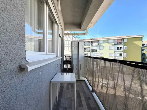 Uski popločani balkon sa bijelim stolom i pogledom na okolne zgrade. - image 9
