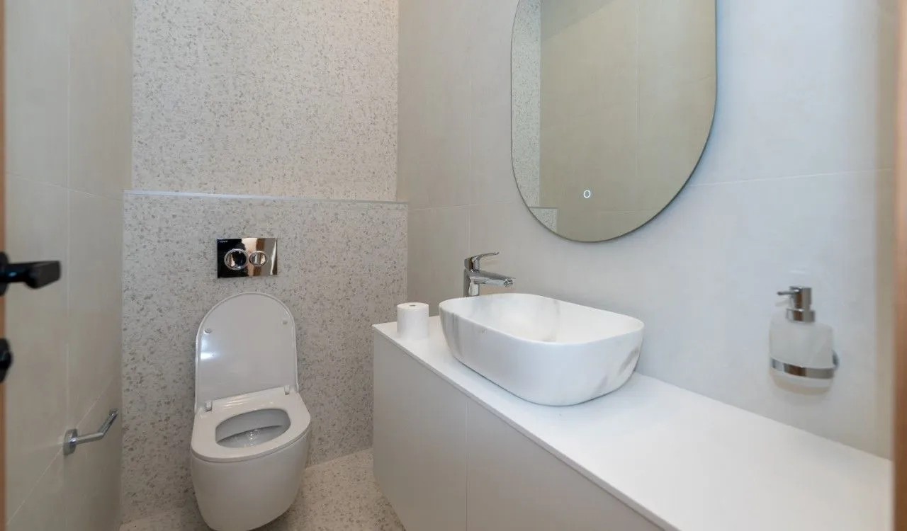 Modernly equipped bathroom with a washbasin, mirror, and toilet.