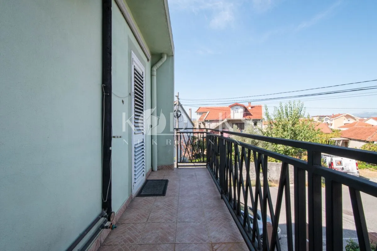 Dugački balkon sa metalnom ogradom i pogledom na okolinu.