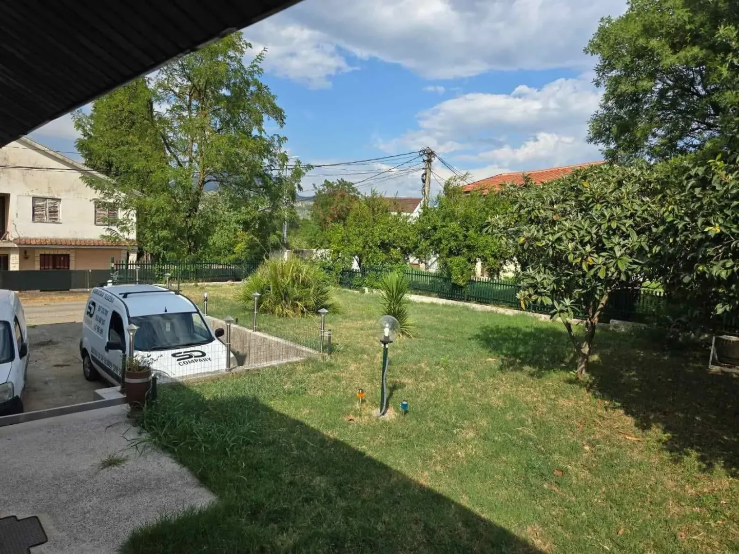 Prostrano dvorište sa zelenim travnjakom, drvećem i popločanim dijelom ispred kuće.