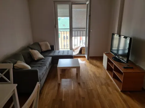 Svijetla dnevna soba sa sivom ugaonom garniturom, televizorom i izlazom na balkon. - image 7