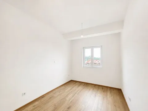 Prazna soba sa bijelim zidovima, drvenim podom i prozorom. - image 10