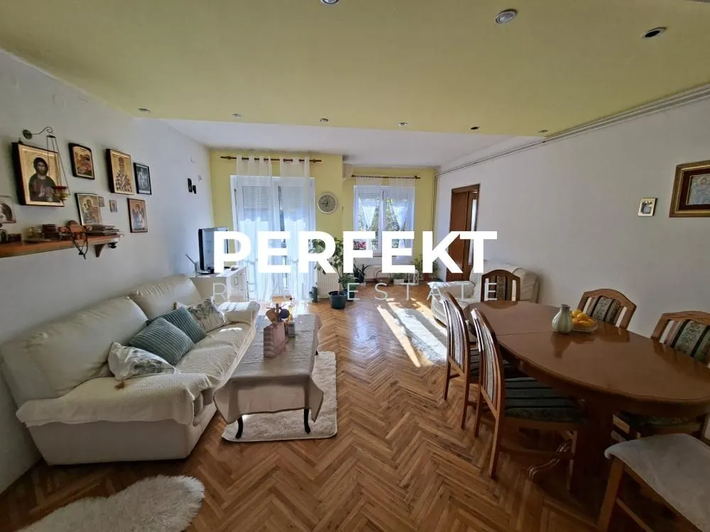 Prostrani dnevni boravak sa garniturom za sedenje i trpezarijskim stolom.