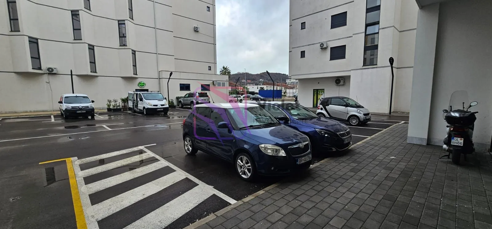 Vanjski prostor sa parkingom ispred stambene zgrade.