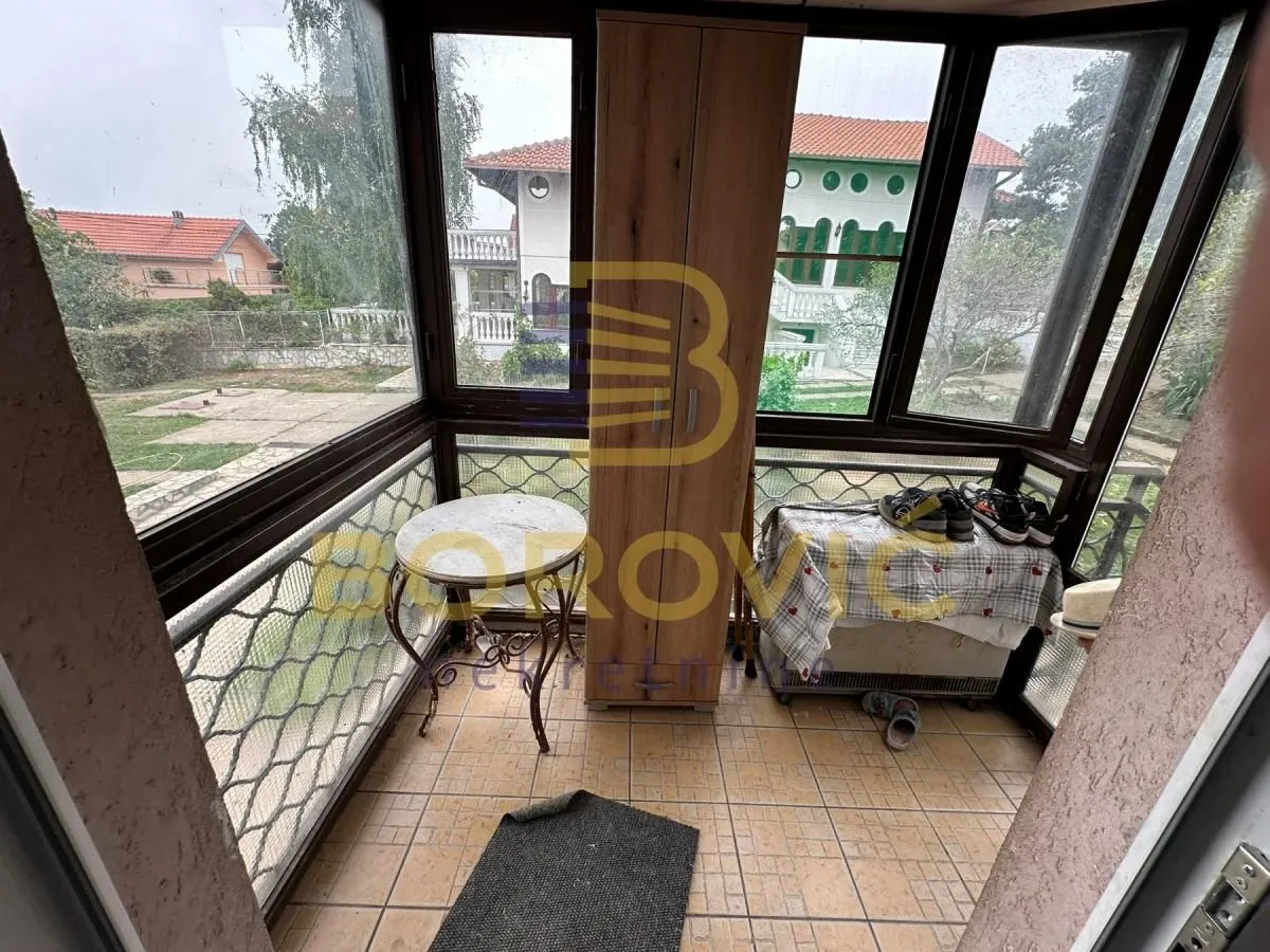 Zastakljena terasa sa pogledom na dvorište i okolne kuće.