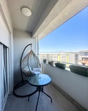 Natkriveni balkon sa stočićem, visećom foteljom i pogledom na okolne zgrade. - image 3