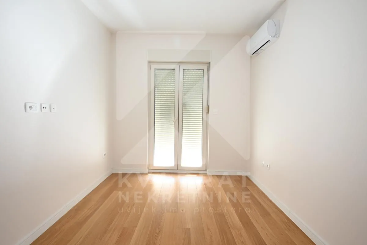 Empty room with wooden flooring, air conditioning unit, and balcony doors.