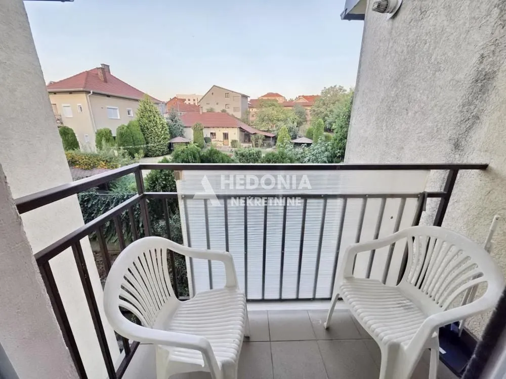 Balkon sa dve plastične stolice i pogledom na naselje i zelenilo.
