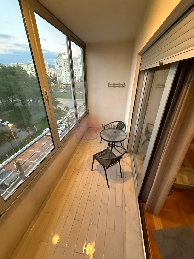 Zastakljeni balkon sa malim stolom i dvije stolice i pogledom na grad.