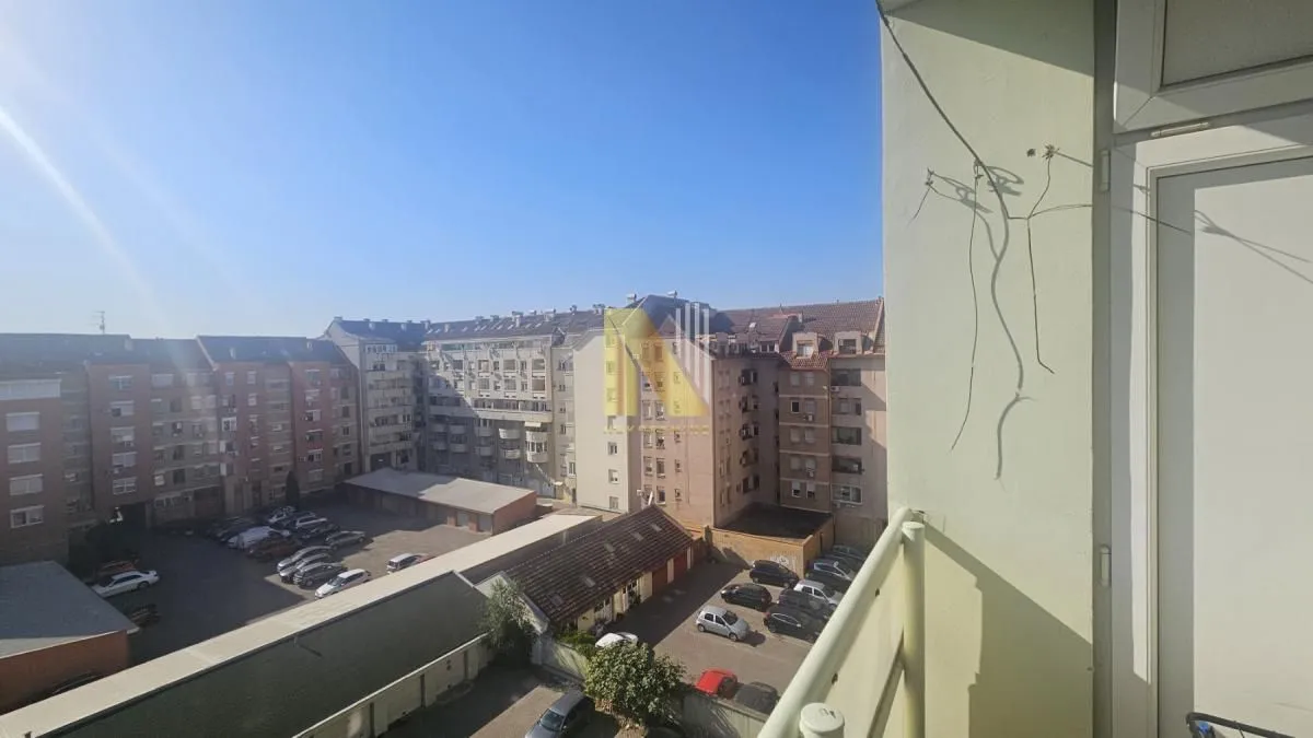 Pogled sa balkona na okolne zgrade i parking.