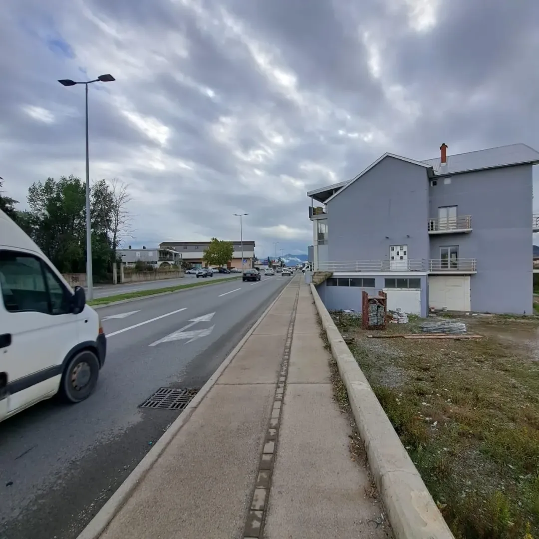 Vanjski izgled višespratne zgrade pored puta sa trotoarom.