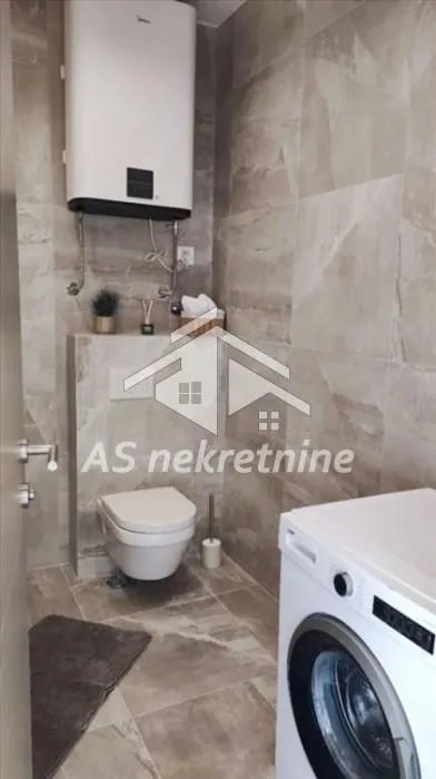 Small tiled bathroom equipped with a toilet, water heater, and washing machine.
