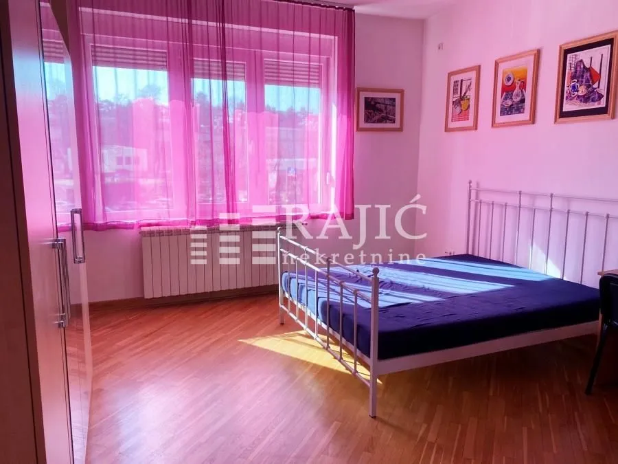 Bedroom with a double bed, wooden floor, and windows with pink curtains.
