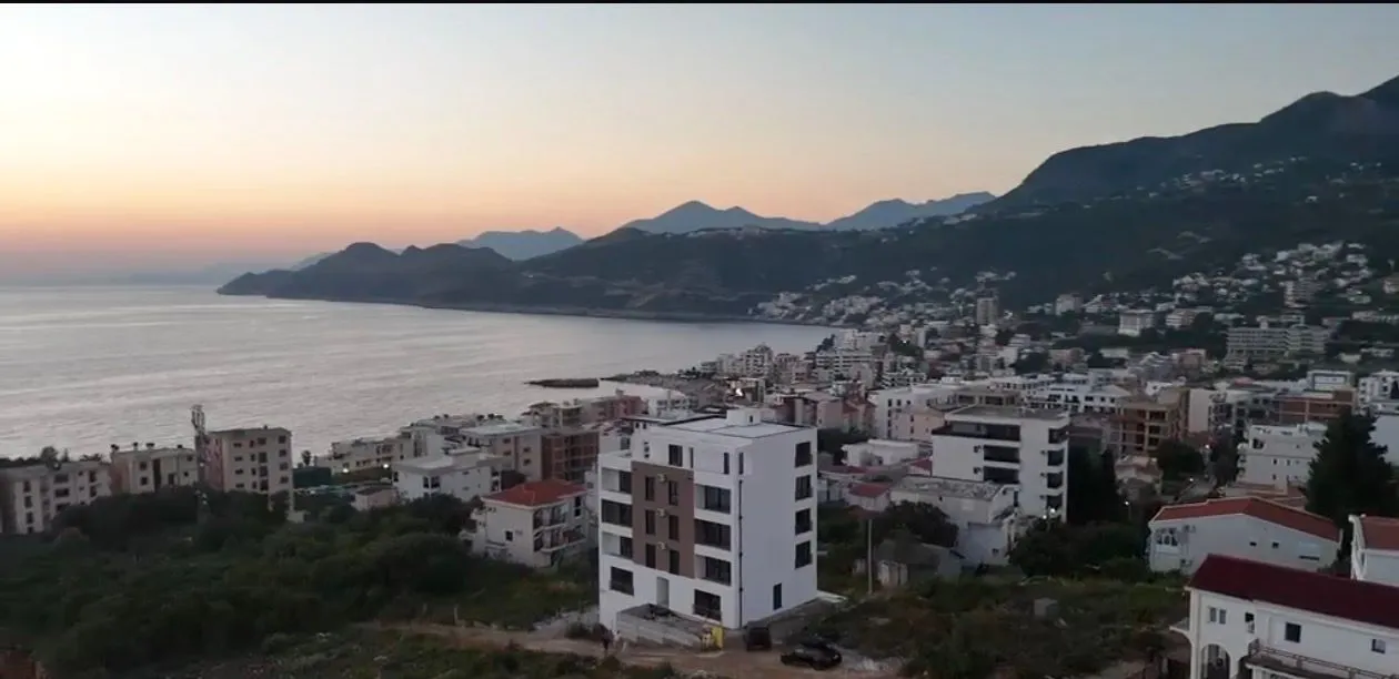 Pogled iz ptičje perspektive na stambenu zgradu i okolno naselje uz obalu mora.