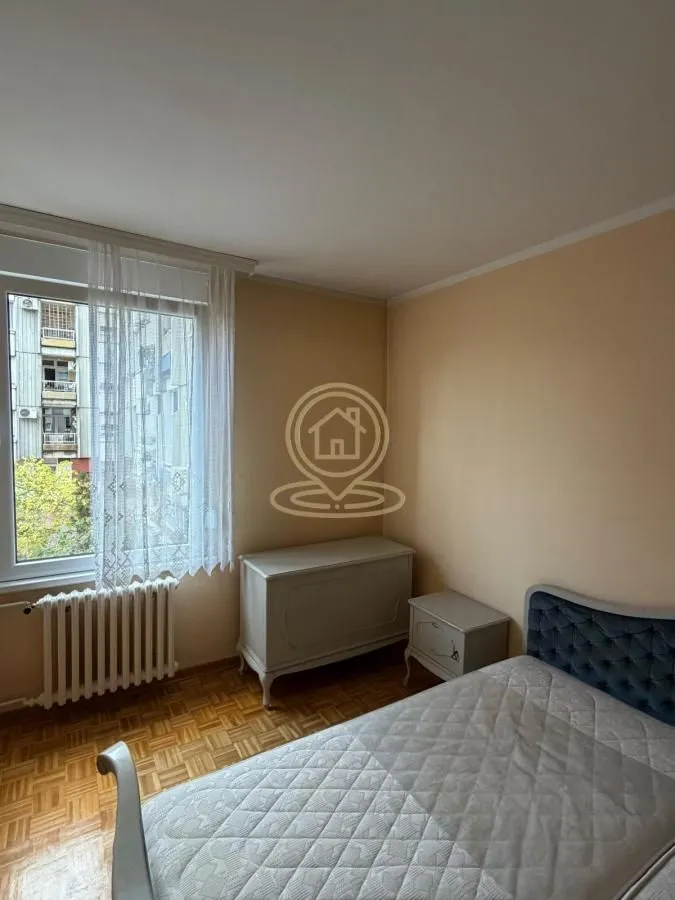 Nameštena spavaća soba sa krevetom, komodom i prozorom.