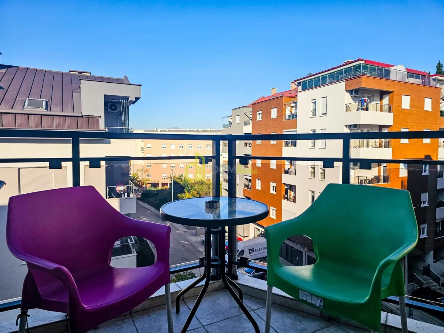 Manji balkon sa stolom i dve stolice i pogledom na naselje.