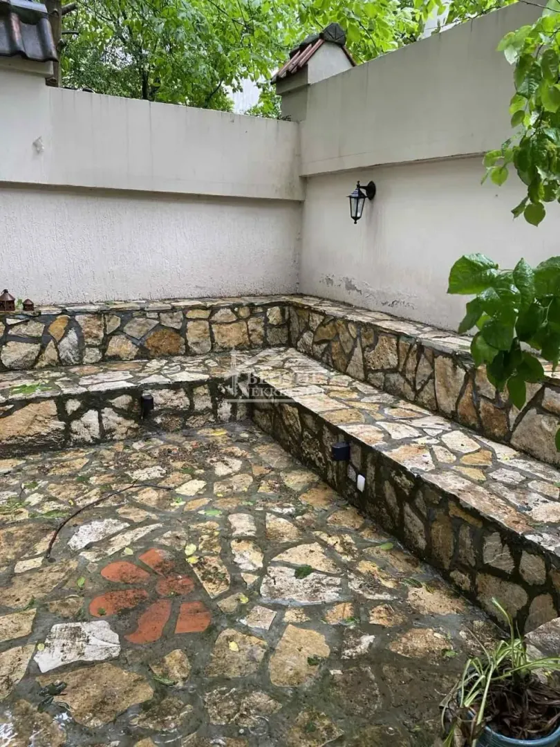 Popločano dvorište sa kamenim klupama i zidom.
