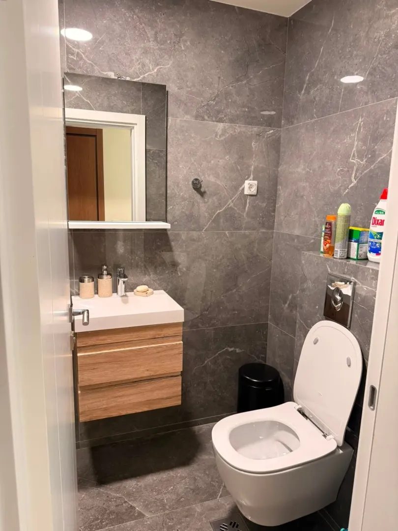 Compact bathroom tiled in grey with a vanity sink and toilet.