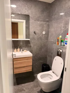 Compact bathroom tiled in grey with a vanity sink and toilet. - image 15