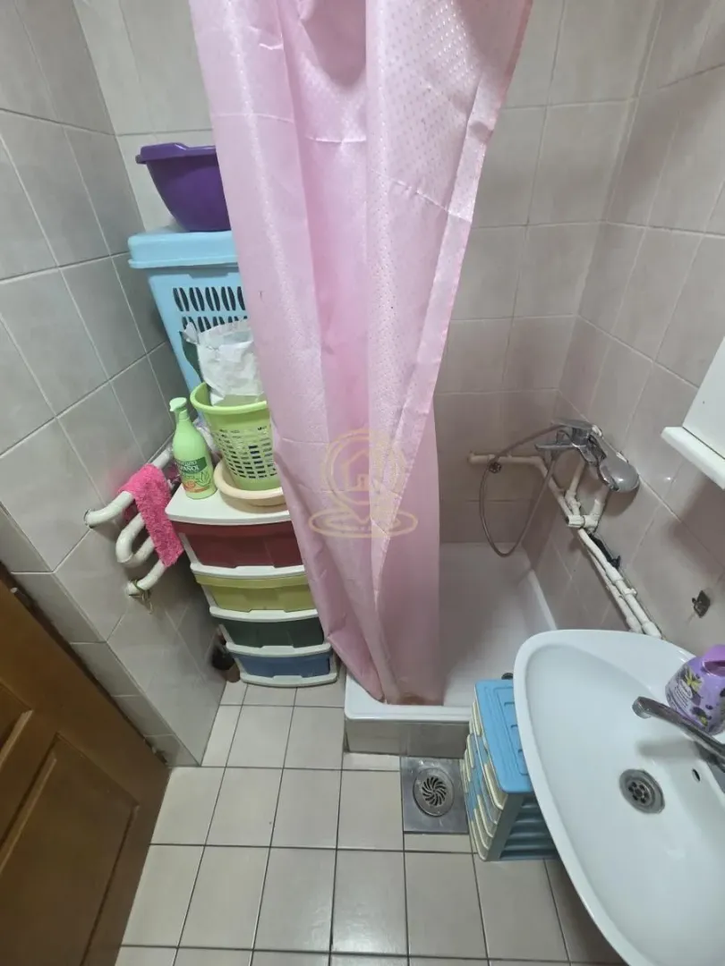 Manje kupatilo sa tuš kabinom, umivaonikom i policama za odlaganje.