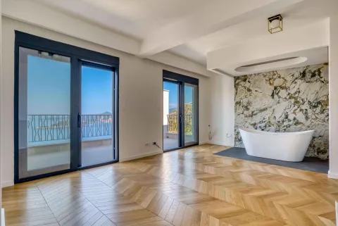 Prostrano kupatilo sa samostojećom kadom, drvenim podom i velikim staklenim vratima koja vode na balkon sa pogledom na more. - image 6