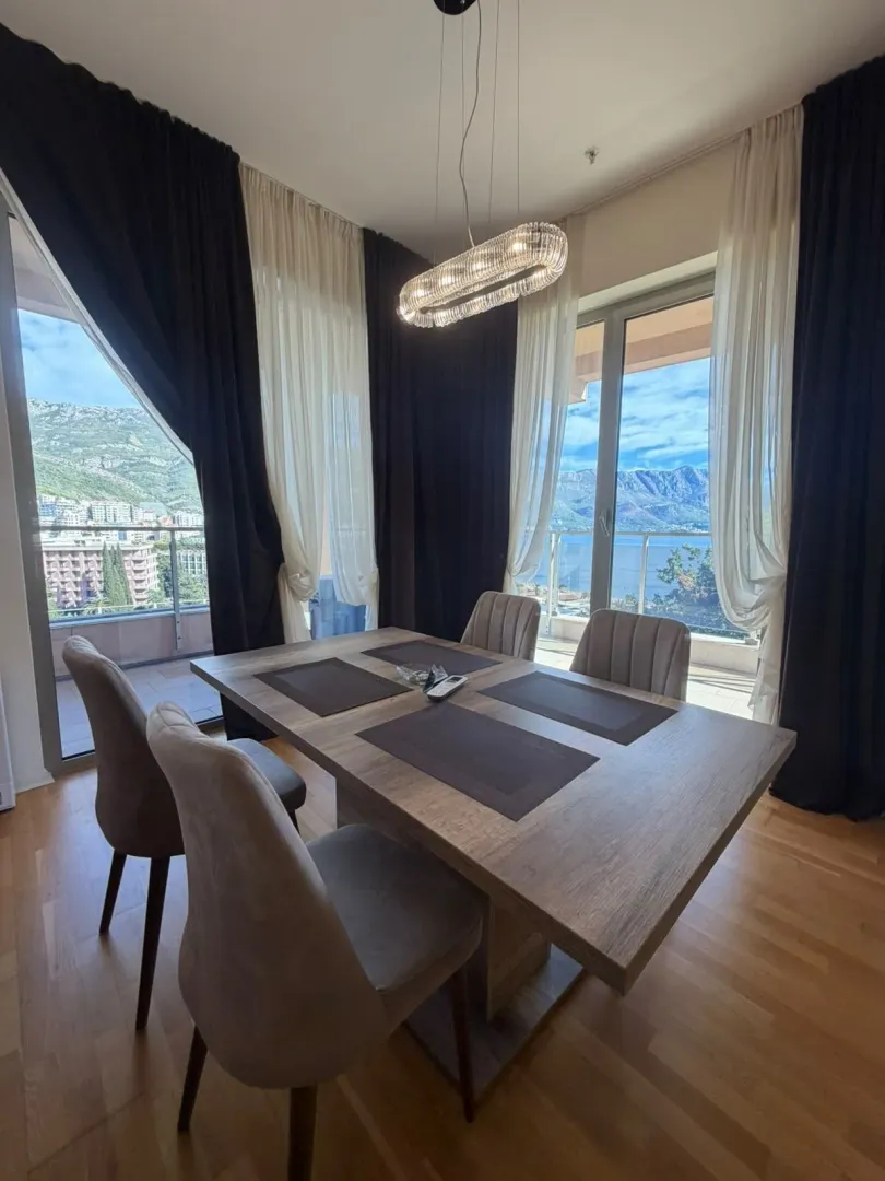 Dining room with a large table and chairs, offering views of the sea and mountains.