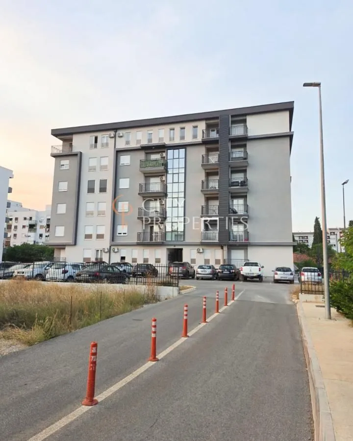 Pogled na spoljašnjost stambene zgrade sa parkingom i prilazom.