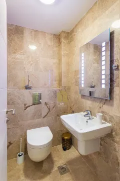 Small bathroom with beige tiles, sink, mirror, and toilet. - image 5