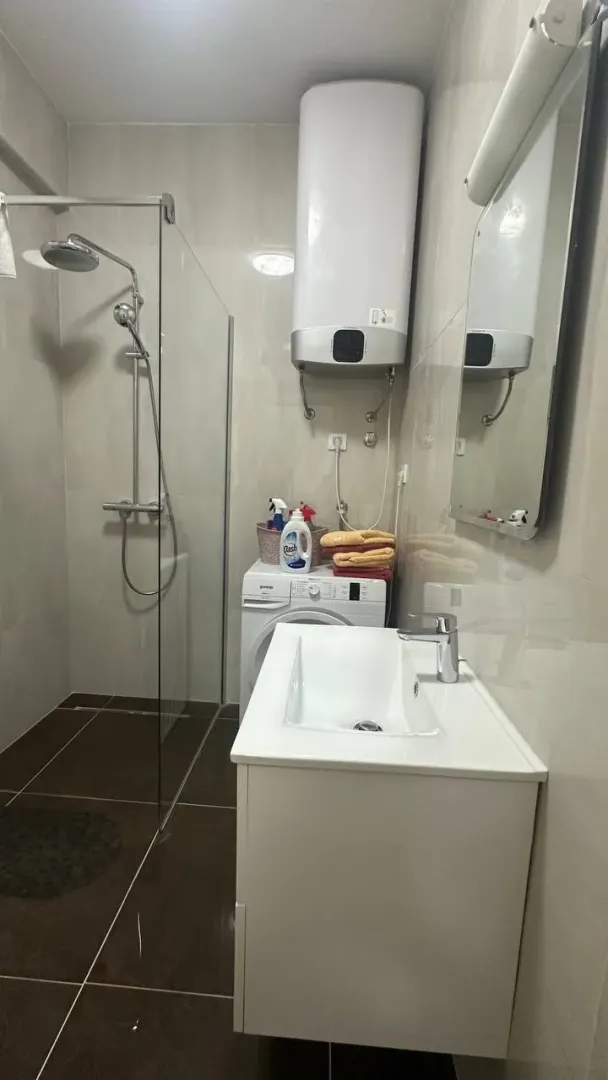 Modern bathroom with a walk-in shower, washbasin, water heater, and washing machine.