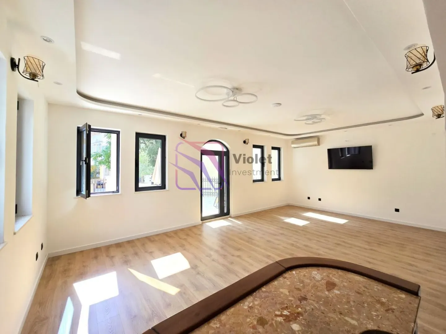 Spacious living room with wooden flooring, large windows and a wall-mounted TV.