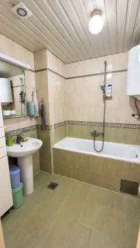 Kupatilo opremljeno kadom, umivaonikom i pločicama u bež i zelenim tonovima. - image 10