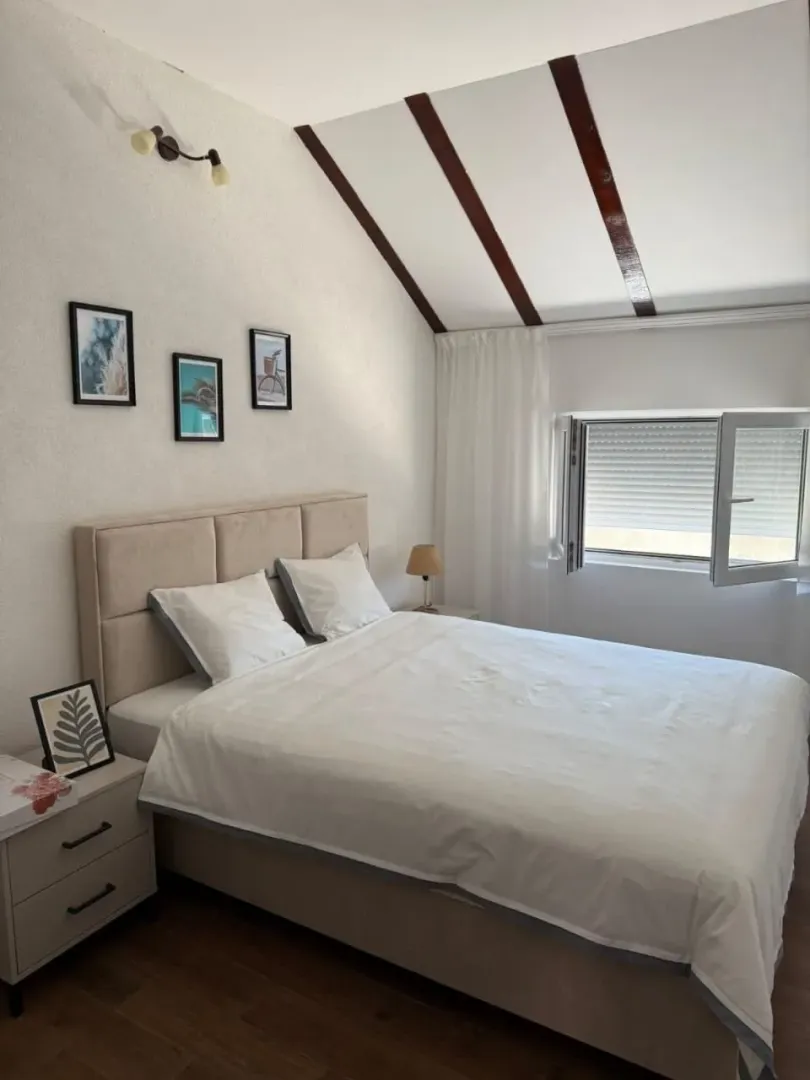Bright bedroom with a double bed, white linens and a window.