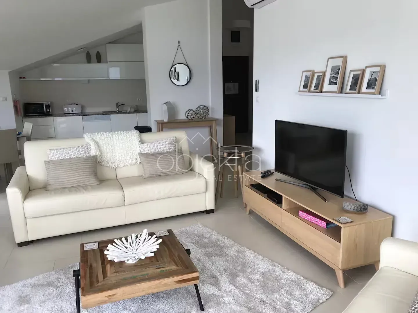 Living room with a sofa, TV, and a view of the kitchen in the background.