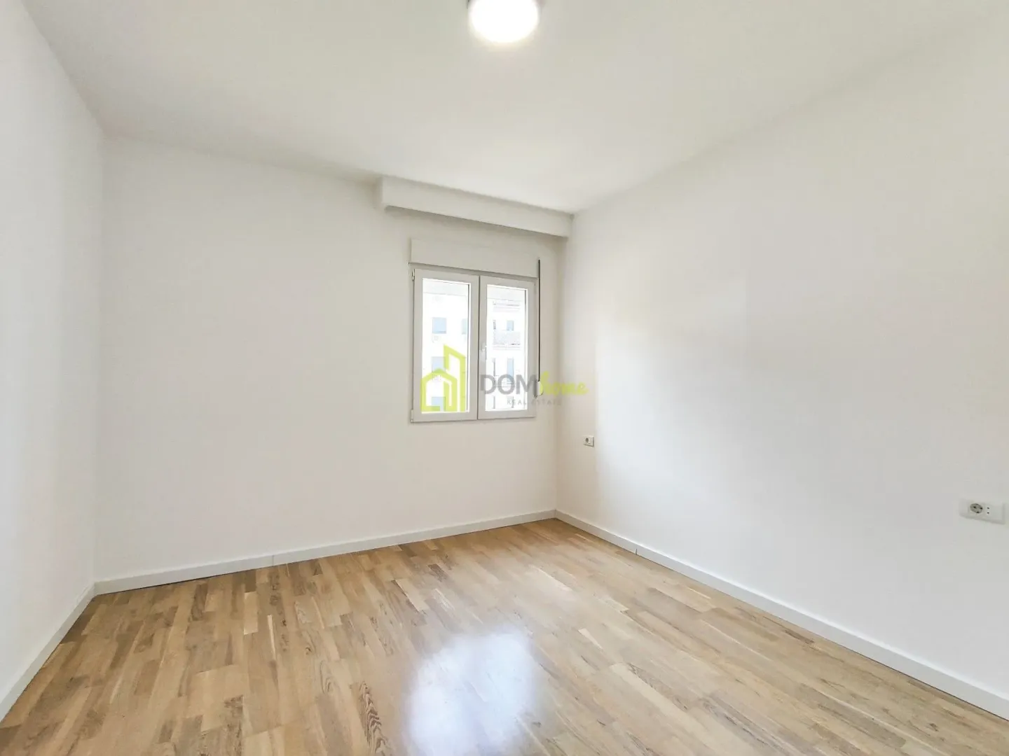 Empty room with white walls, wooden parquet flooring and a window.