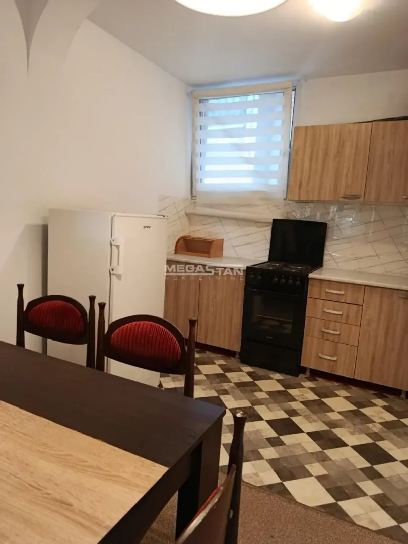 Manja kuhinja sa drvenim elementima, šporetom, frižiderom i trpezarijskim stolom.