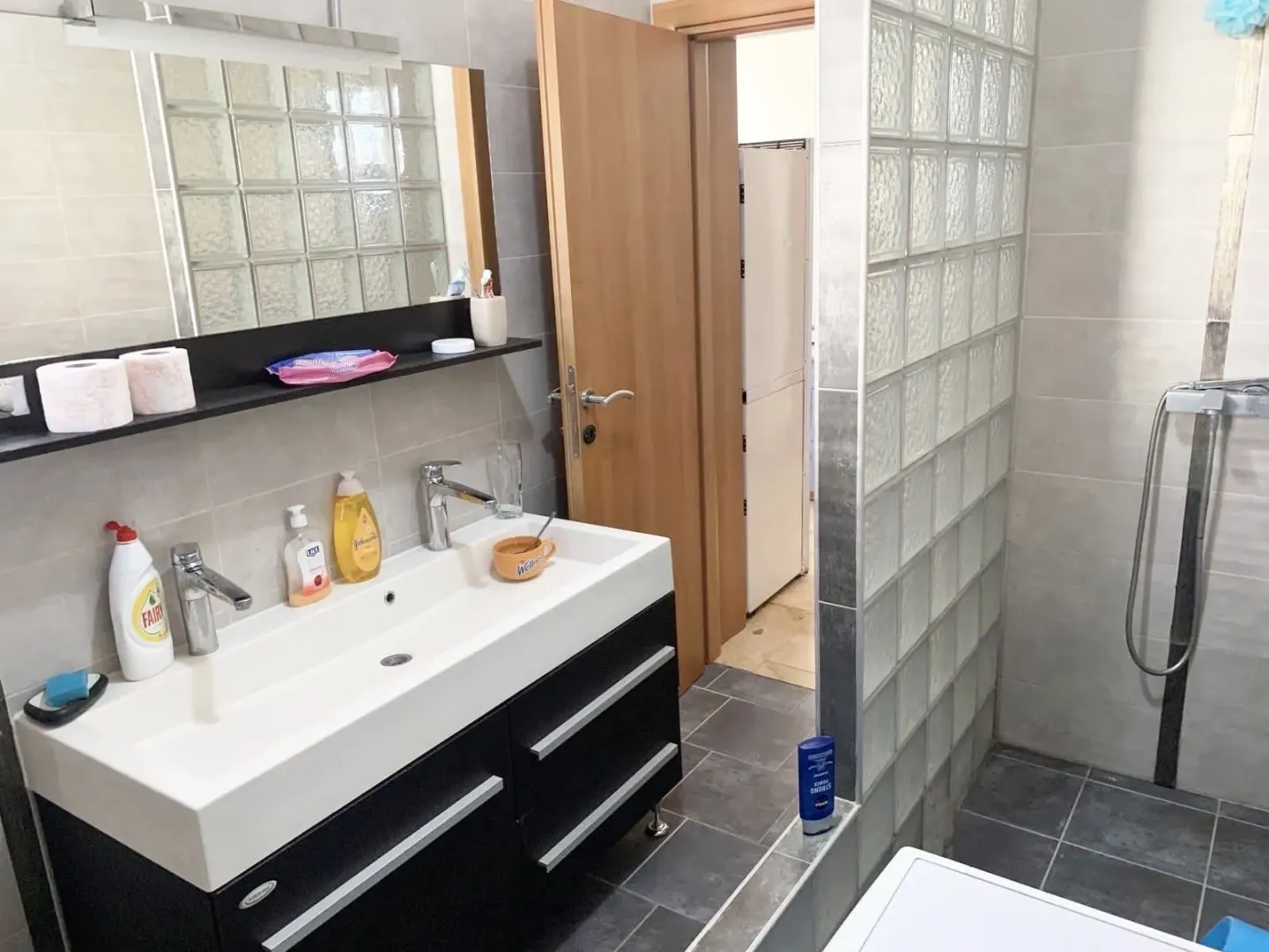 Bright bathroom featuring a double faucet sink and a glass block wall.