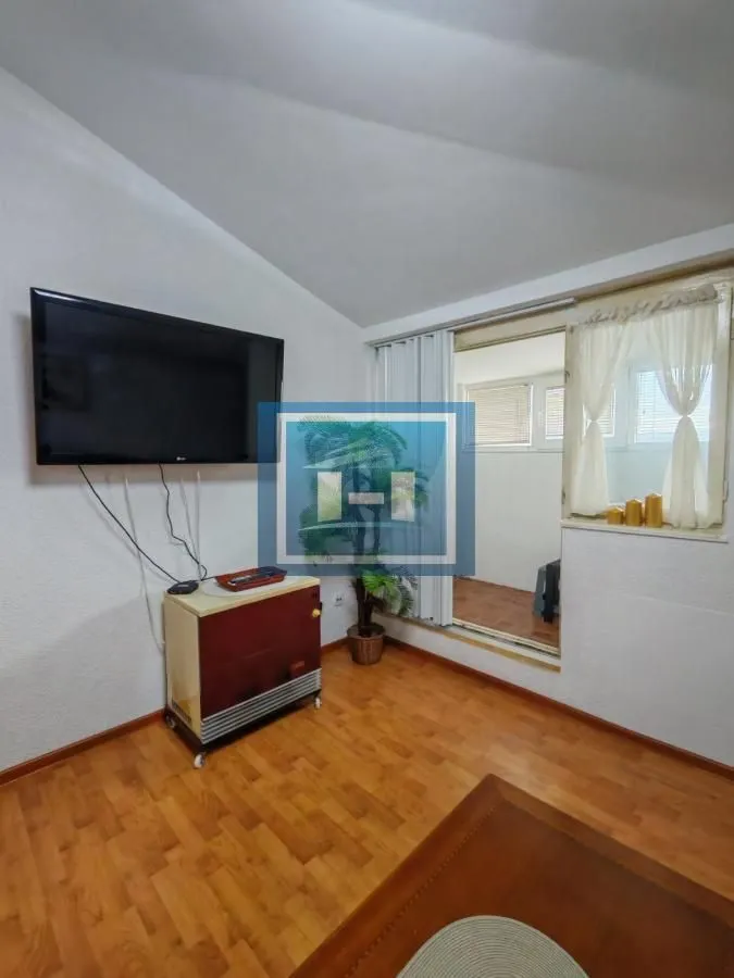 Living room with wooden flooring, wall-mounted TV, and access to the terrace.