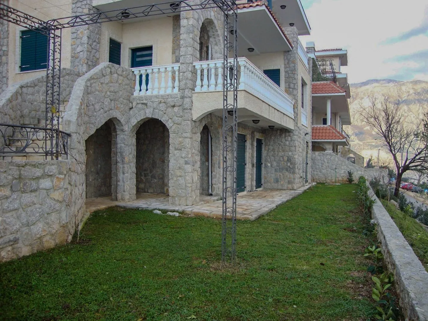 Eksterijer kuće sa kamenom fasadom, balkonom i uređenim dvorištem.