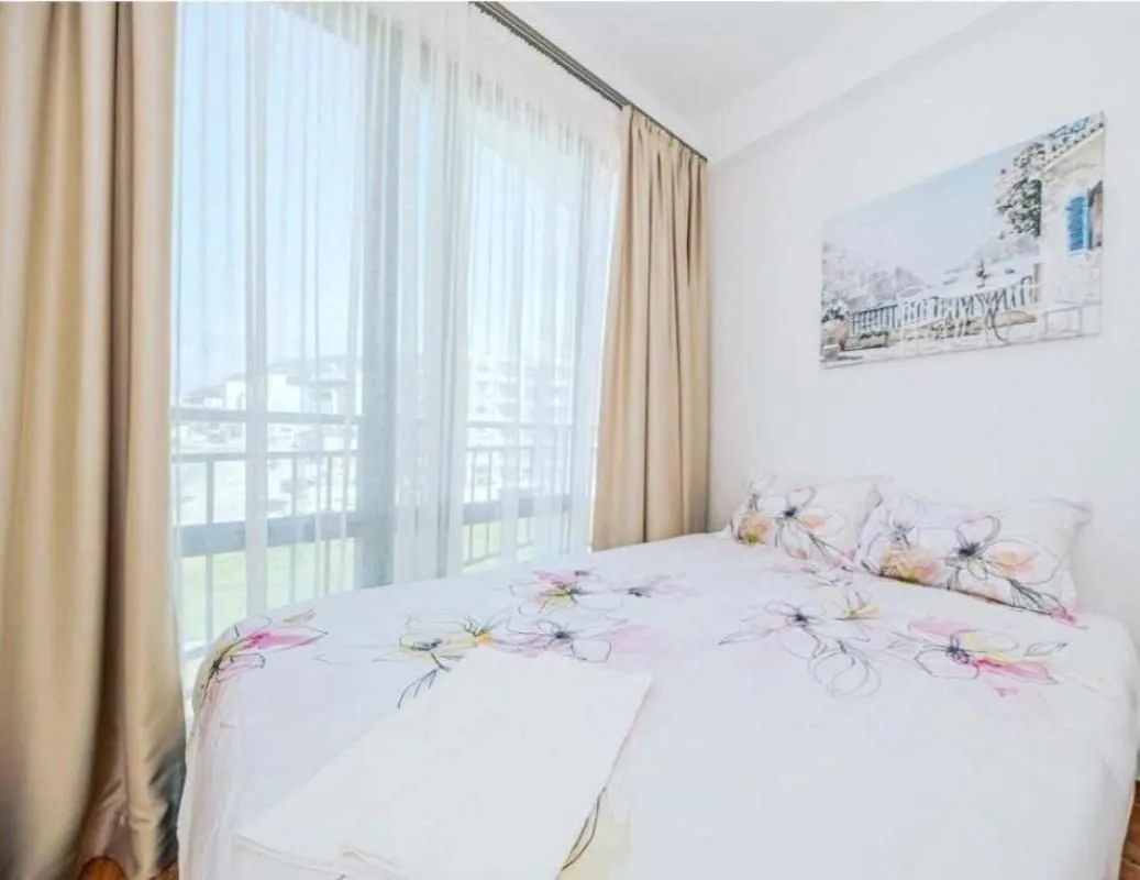 Bedroom with a double bed, floral bedding, and a large window with light curtains.