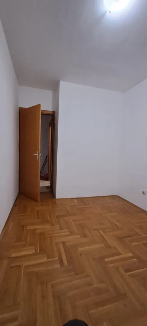 Prazna soba sa parketom i otvorenim drvenim vratima.