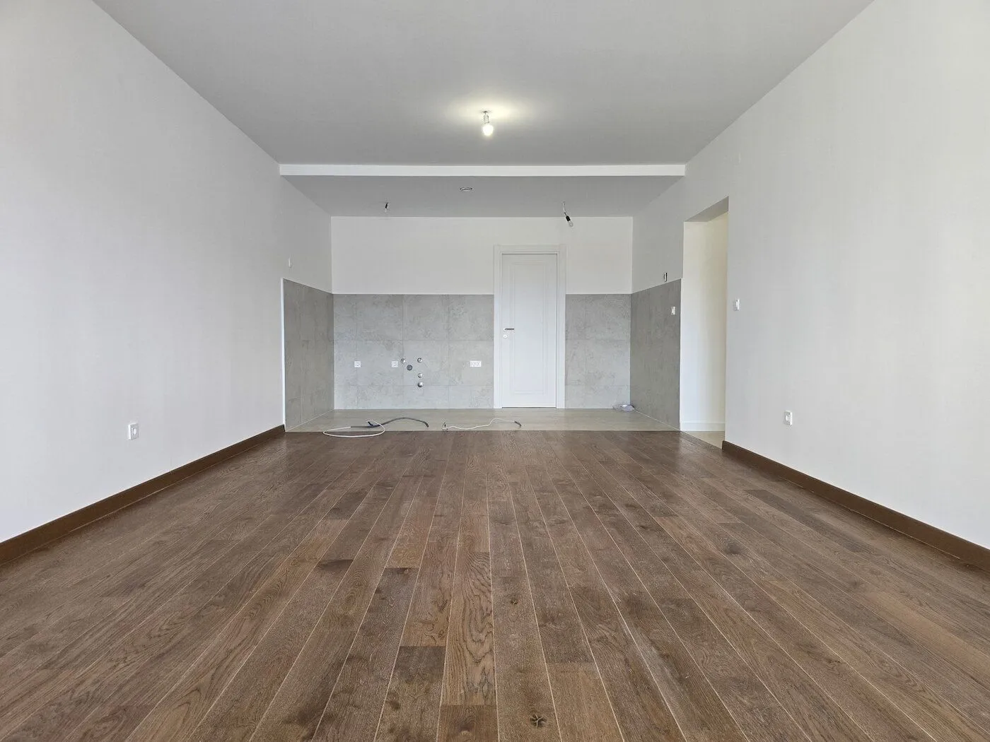 Empty room with laminate flooring and a designated kitchen area.