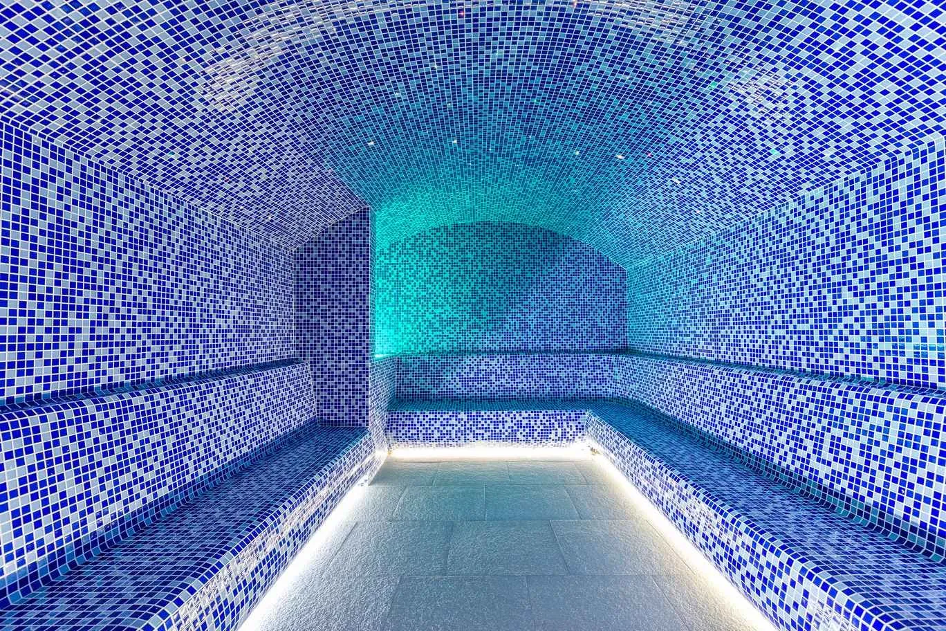 Modern steam room tiled with blue mosaic tiles.