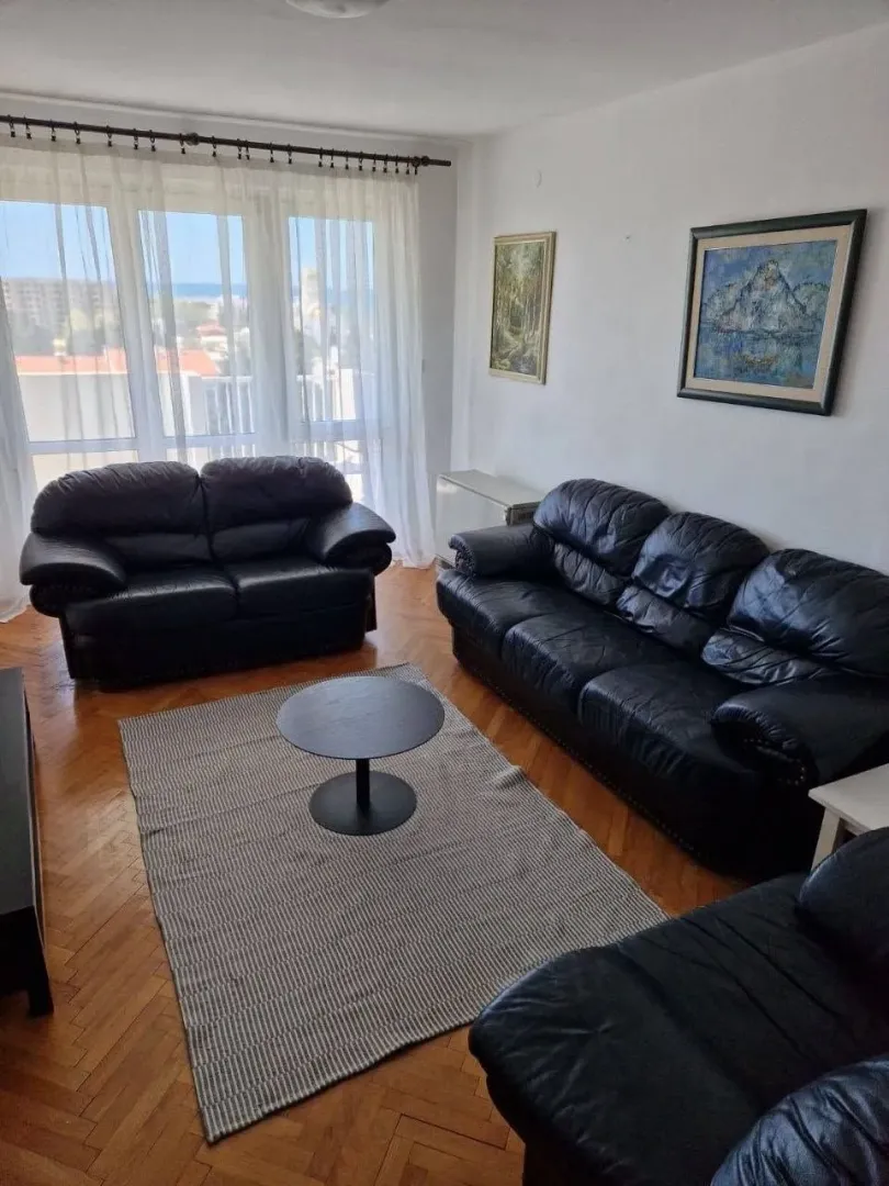 Living room with black leather sofas, a rug, and a large window.