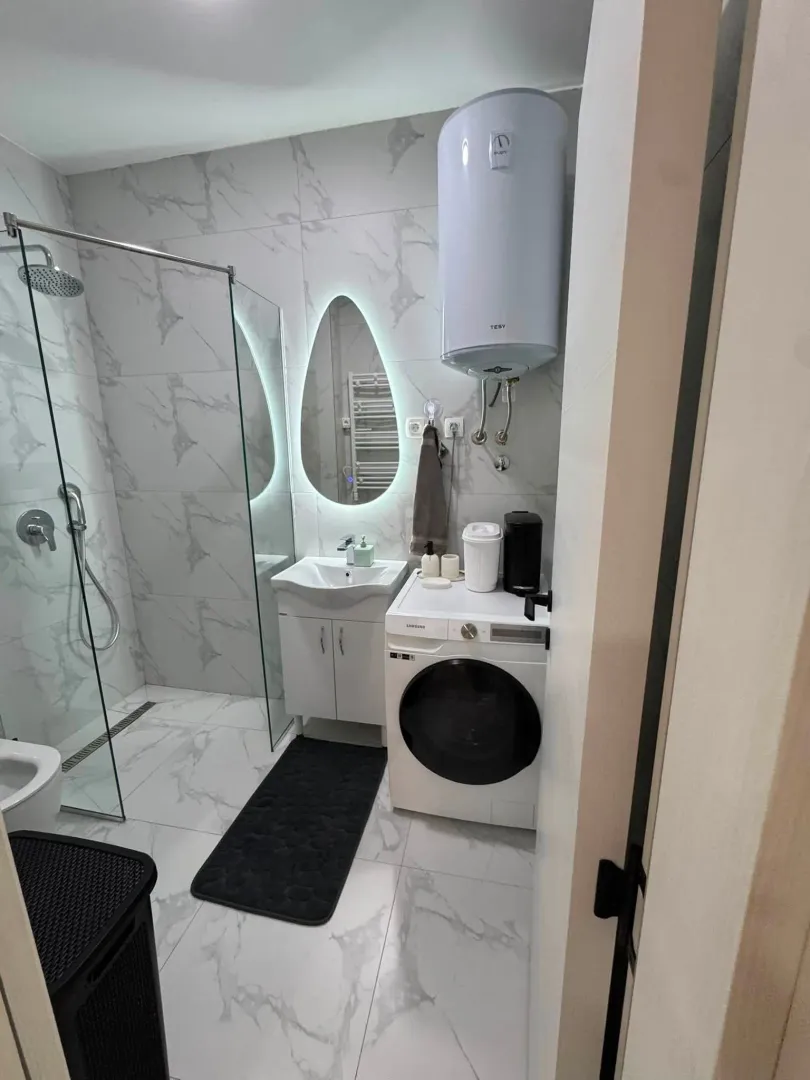Modernly equipped bathroom with a walk-in shower, washbasin, and washing machine.