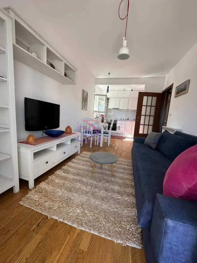 Dnevna soba sa garniturom, TV-om i pogledom na kuhinju u pozadini.