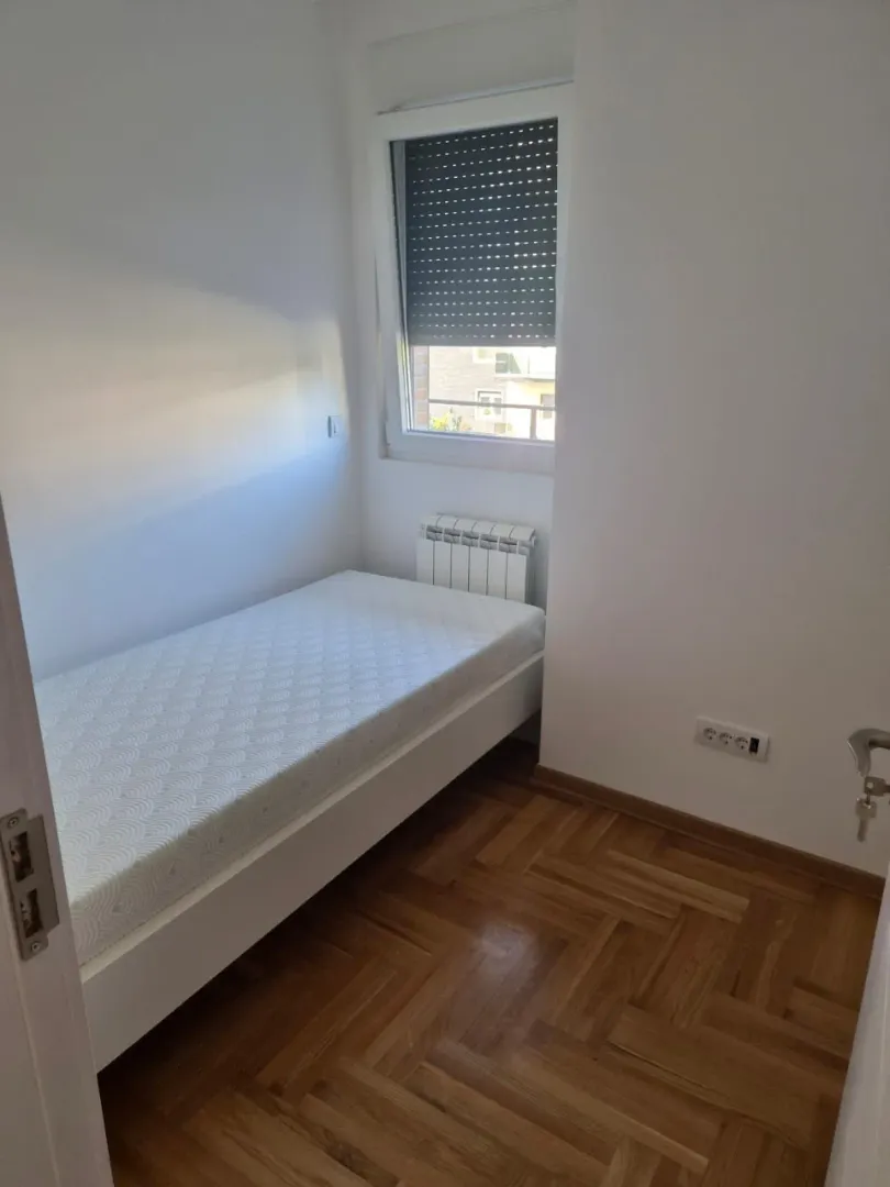 Manja spavaća soba sa krevetom, parketom i prozorom.