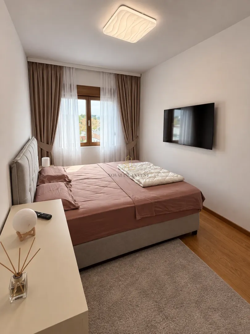 Modern bedroom with a double bed, wall-mounted TV, and window with curtains.